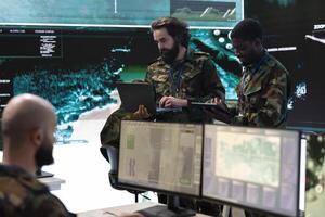 Military staff briefing the new recruits in military headquarters control room, operating with a big screen to monitor CCTV reconnaissance footage. Soldiers collecting data in power base. photo
