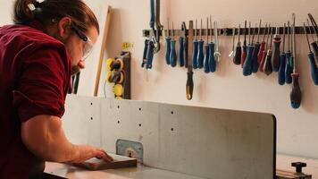 Man putting on protection gear while inserting plank in spindle moulder to prevent workplace accidents. Carpenter equipping safety glasses while cutting lumber with wood shaper, camera A photo