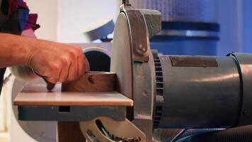 Artisan sanding wooden object on disc sander in assembling shop. Diy hobby enjoyer working in joinery, guiding wood against grinding machine rotating disc to create art, camera A close up shot photo