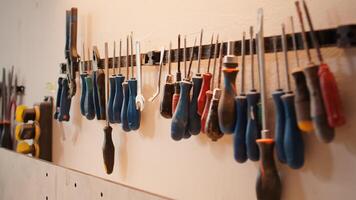 Chisels, screwdrivers, wrench and pliers on wall in furniture assembly shop, panning shot. Close up of various woodworking tools on rack in joinery used for working with wood materials photo