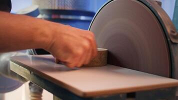 Artisan sanding wooden object on disc sander in assembling shop. Diy hobby enjoyer working in joinery, guiding wood against grinding machine rotating disc to create art, camera B close up shot photo