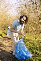 Proud environmentalist collecting rubbish to fight against pollution within the forest habitat, protecting the ecosystem. Volunteer doing community service to clean the woods from trash. photo