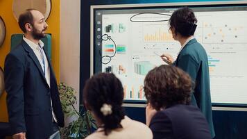 Project team reviewing monthly reports and data on interactive board, studying market trends and customer needs to ensure objectives fulfillment. Workers accomplish business goals. Camera A. photo