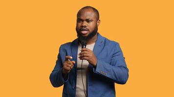 African american motivational speaker holding monologue using microphone, gesturing with hands, studio background. Energetic BIPOC speaker talking during presentation using mic, doing speech, camera A photo