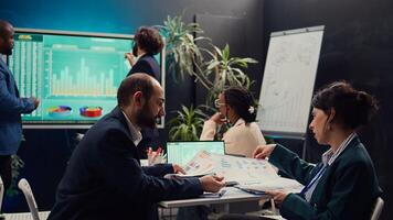 Public relations team creating marketing campaigns and promotional activities in a boardroom, collaborating on new development plan. Employees reviewing sales trends metrics on pc. Camera B. photo