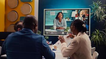 Project management team attending videocall meeting with shareholders, creating a presentation to review updates and data reports. Employees discuss remotely with executive board members. Camera B. photo