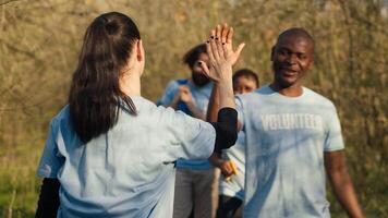 Activists congratulating each other with a high five after a successful teamwork, showing perseverance in collecting rubbish and plastic waste from forest environment. A job well done. Camera A. photo