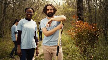 Portrait of two activists clearing up the forest surroundings by collecting garbage, growing new trees and picking up trash. Eco friendly enthusiasts preserving environments and wildlife. Camera B. photo