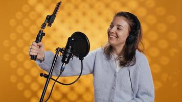 Joyous influencer filming herself reviewing book with selfie stick, isolated over studio background. Woman doing vlog with self portrait camera, talking with audience about novel, camera B photo
