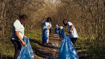 Diverse activists cleaning up rubbish in a garbage disposal bag, environmental conservation concept. Volunteers protecting the forest ecosystem, collecting rubbish with claw tool. Camera B. photo
