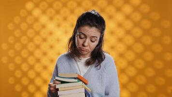 Portrait of woman browsing through stack of textbooks, gathering information for school exam, isolated over studio background. Person searching necessary course for exam in pile of books, camera B photo
