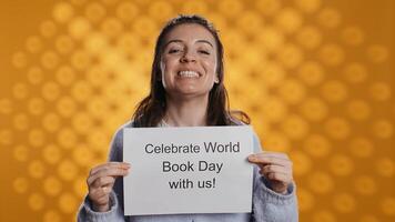 Portrait of happy woman holding placard with world book day message written on it, isolated over studio background. Geek promoting importance of reading during 23th April global event, camera B photo