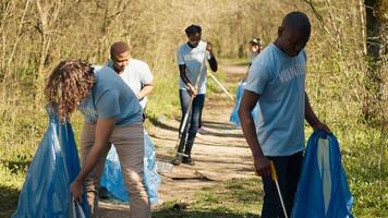 Diverse men volunteers pick up rubbish and plastic trash with tongs, working to combat illegal dumping and preserve natural forest environment. Activists volunteering for litter cleanup. Camera A. photo
