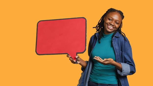 Smiling woman holding red speech bubble sign of empty copy space for message. Joyous person presenting thought bubble cardboard used as promotion concept, isolated over studio background, camera A photo