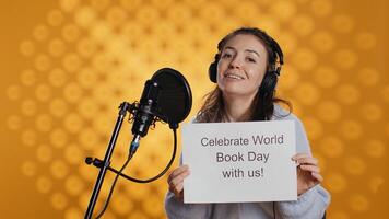 Smiling woman filming promotional for world book day, isolated over studio background. Influencer promoting reading, gaining awareness for international global event, camera B photo