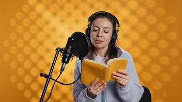 Narrator wearing headphones, reading aloud from book into microphone, exhaling after finally finishing job. Person recording audiobook, creating engaging media content for listeners, camera B photo