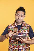 Man adding payment method on shopping website using tablet, taking advantage of promotions, studio background. Indian person buying stuff online using credit card, typing data on device photo