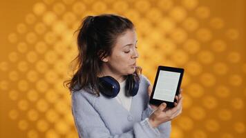 Portrait of smiling woman showing ebook reader to interested customers, doing advertisement. Radiant person doing promotion for reading tablet, showing features, studio background, camera B photo