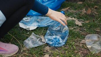 Diverse volunteers collecting trash and storing in the garbage bag, picking up junk and plastic waste to help with forest pollution. Clearing the woods, ecosystem protection. Close up. Camera A. photo
