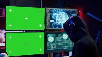 Hacker using isolated screen monitor and artificial intelligence to write spyware software, listening music. Scammer wearing headphones using AI and chroma key PC to do fraud using AI, camera B photo