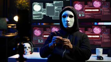 Hacker group member wearing anonymous mask filming threatening another country government to steal military secrets, doing international espionage in hidden underground base, camera A photo