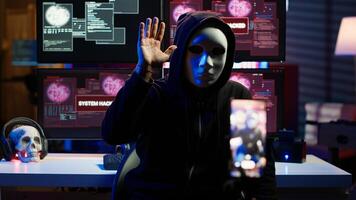 Hacker concealing identity filming ransom in hidden underground base, threatening to release stolen data publicly if payout demands are not met, using phone to record blackmail footage, camera A photo