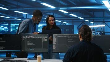 Manager overseeing server room using laptop to do hardware troubleshooting, talking with multiracial employees. Supervisor doing inspection in data center, receiving performance assessment from worker photo