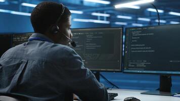 IT support worker in data center talking in headset mic with coworkers, coding on computer. Man discussing with colleagues using headphones microphone, overseeing server clusters photo