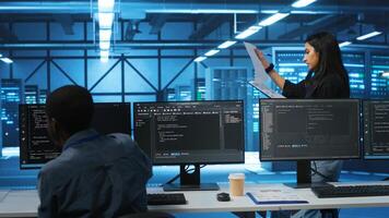 Indian manager in data center doing inspection on electronics and workers, ensuring order. Team leader reading clipboard files, supervising employees in server room infrastructure components photo