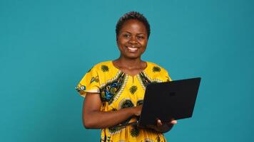 Young woman freelancer navigating on online webpages in studio, browsing information on device connected to internet. Charming traditional girl carries a portable pc. Camera A. photo