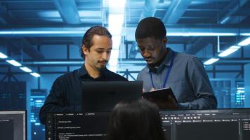 Multiethnic coworkers in server room collaborating to fix servers providing computing resources for workloads. Diverse team of admins supervising data center supercomputers photo