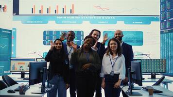 Confident smiling enterprise team uniting their forces to improve workflow and efficiency, achieve organizational goals. Diverse group of analysts work in telecommunications control room. Camera B. photo