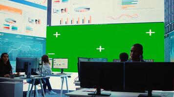 Diverse group of business specialists solve their daily tasks in control room with big greenscreen, analyzing big data numbers to ensure organizational progress. Startup management team. Camera B. photo