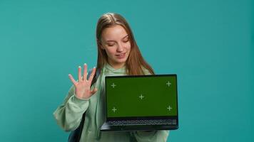 Smiling woman presenting laptop with green screen display, isolated over blue studio background. Cheerful person creating promotion with chroma key notebook device, camera A photo