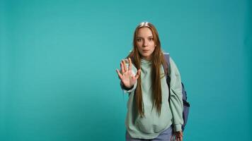 Assertive young woman doing stop hand gesture and talking. Annoyed girl doing firm halt sign gesturing, wishing to end concept, isolated over blue studio background, camera B photo