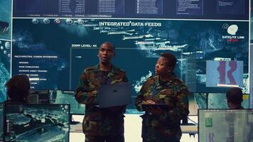 Sergeant major and female soldier checking real time field data in command post monitoring room, examining missions and operations. Team of troops interprets satellite imagery. Camera B. photo