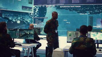 Platoon captain handling surveillance and safety operations with crew, dashboard to oversee field missions within enemy territory. Soldiers monitor CCTV satellite footage on big screen. Camera B. photo