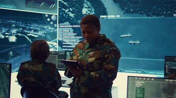 Female military officer supervising radar surveillance footage to input and process tactical data on a big screen. Woman uses global reconnaissance in creating battlefield maps. Camera B. photo