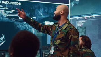 Commander managing cybersecurity measures to protect federal data from enemy breaches, working with his crew from a control center military base. Army officer ensures national safety. Camera A. photo