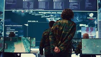 Military surveillance officers talking next to a big screen in general headquarters for cyber operations, control and monitoring to manage national security and army communications. Camera B. photo