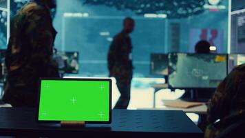 Tablet with greenscreen display running in a command post base of operations, military personnel ensuring national safety in control room. Soldiers and commanders use radar surveillance. Camera B. photo