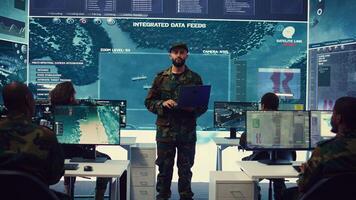 Special operations soldier allocating resources to different units based on mission needs, examines strategic data on a big screen in military control center. Marine corps troops. Camera B. photo