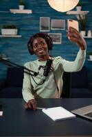 Woman content creator holding smartphone smiling at camera while taking selfie filming vlog. Social media vlogger recording podcast answering subscribers questions using production equipment photo