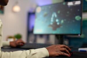 Close-up of professional successful gamer holding hand on computer mouse playing space shooter games during online championship. Pro player woman using RGB gaming equipment in home studio photo