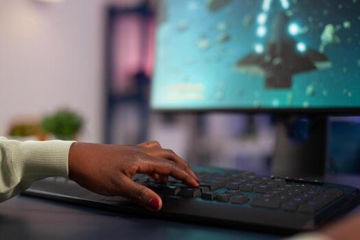 Close up of successful pro gamer pressing computer keyboard while playing space shooter videogames during online championship. Woman player sitting at desk in gaming studio using RGB equipment photo
