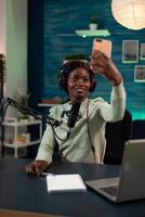 African american vlogger smiling while taking selfie using modern smartphone during live stream. Social media creator recording tutorial using vlogging production equipment. On air talk photo