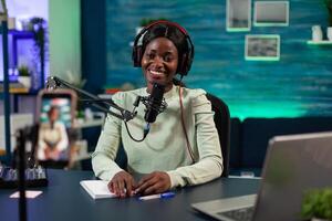 African american influencer woman smiling while recording content using modern smartphone for social media. Vlogger person talking with youtube answering subscribers questions photo