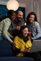 Multi-ethnic friends relaxing on couch laughting while watching fuuny comedy film during movie night at home enjoying spending time together. Group of people hanging out in evening. Friendship concept photo