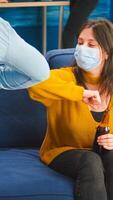 Happy cheerful friends touching elbow keeping social distancing greeting each other wearing face mask preventing spread of coronavirus, holding beer bottles socializing in apartment living room photo