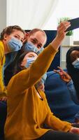 Multiracial friends taking selfie with face masks during covid 19 outbreak, new normal lifestyle concept with people having fun in living room respecting social distance to prevent virus spread photo